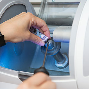 Person adjusting a device with blue light, likely in a lab or manufacturing setting.