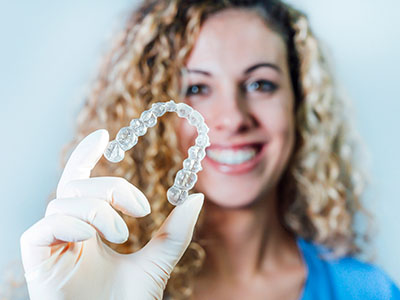 The image shows a person holding up a transparent plastic dental retainer with a smile, displaying its shape and size.