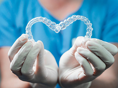 An image of a hand holding a heart-shaped dental retainer with a transparent background, showcasing the item against a blue backdrop.