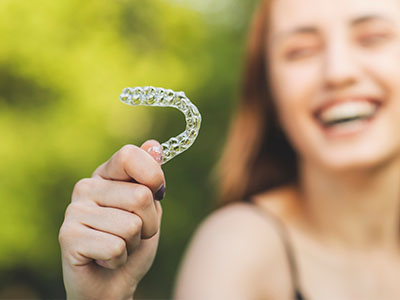 A young woman holding a clear plastic toothbrush with bristles, smiling and looking towards the camera.